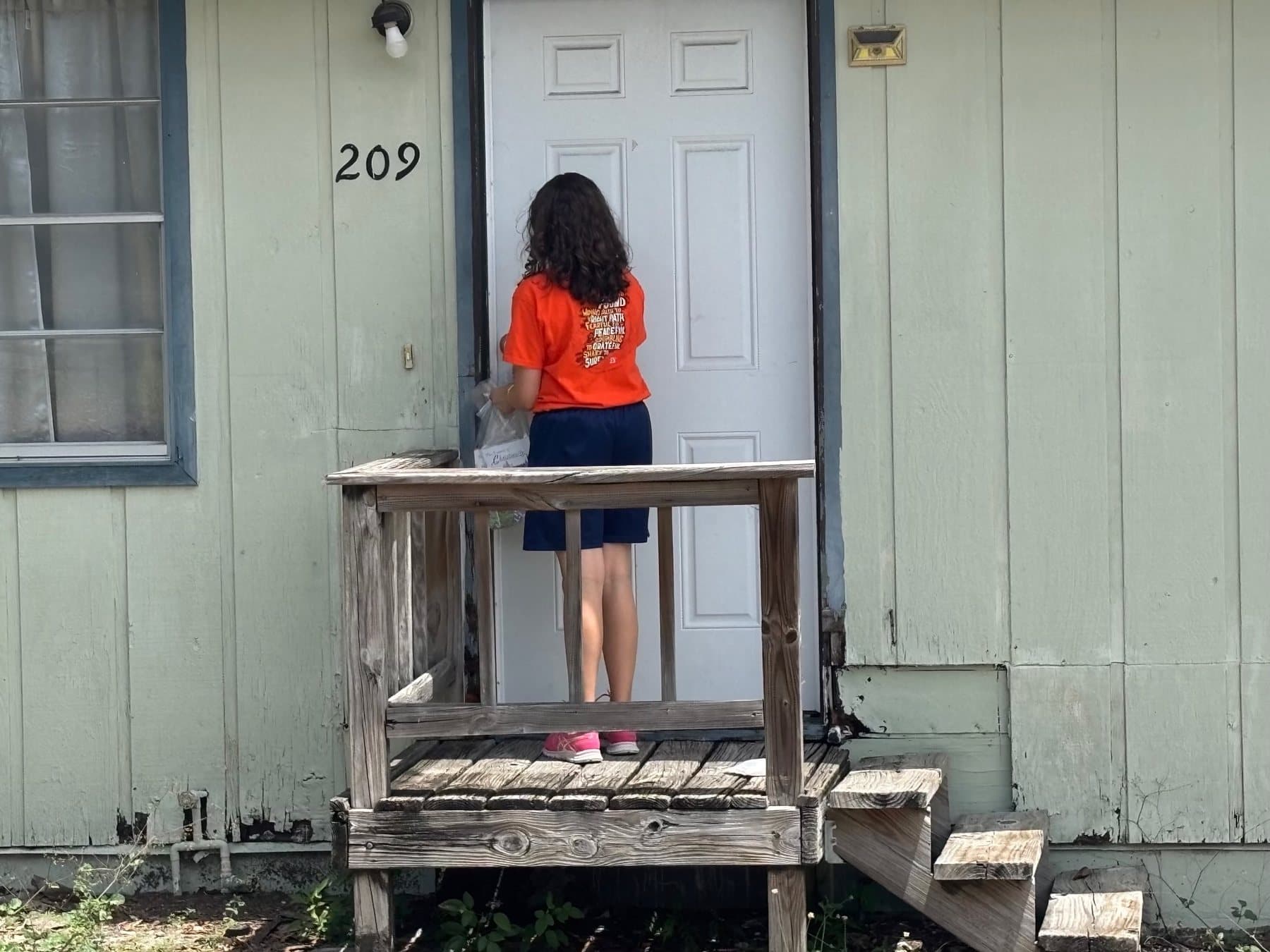 A girl in an outreach shirt at a front door, inviting a neighbor to church
