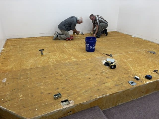 Two men on their knees laying subfloor on the platform