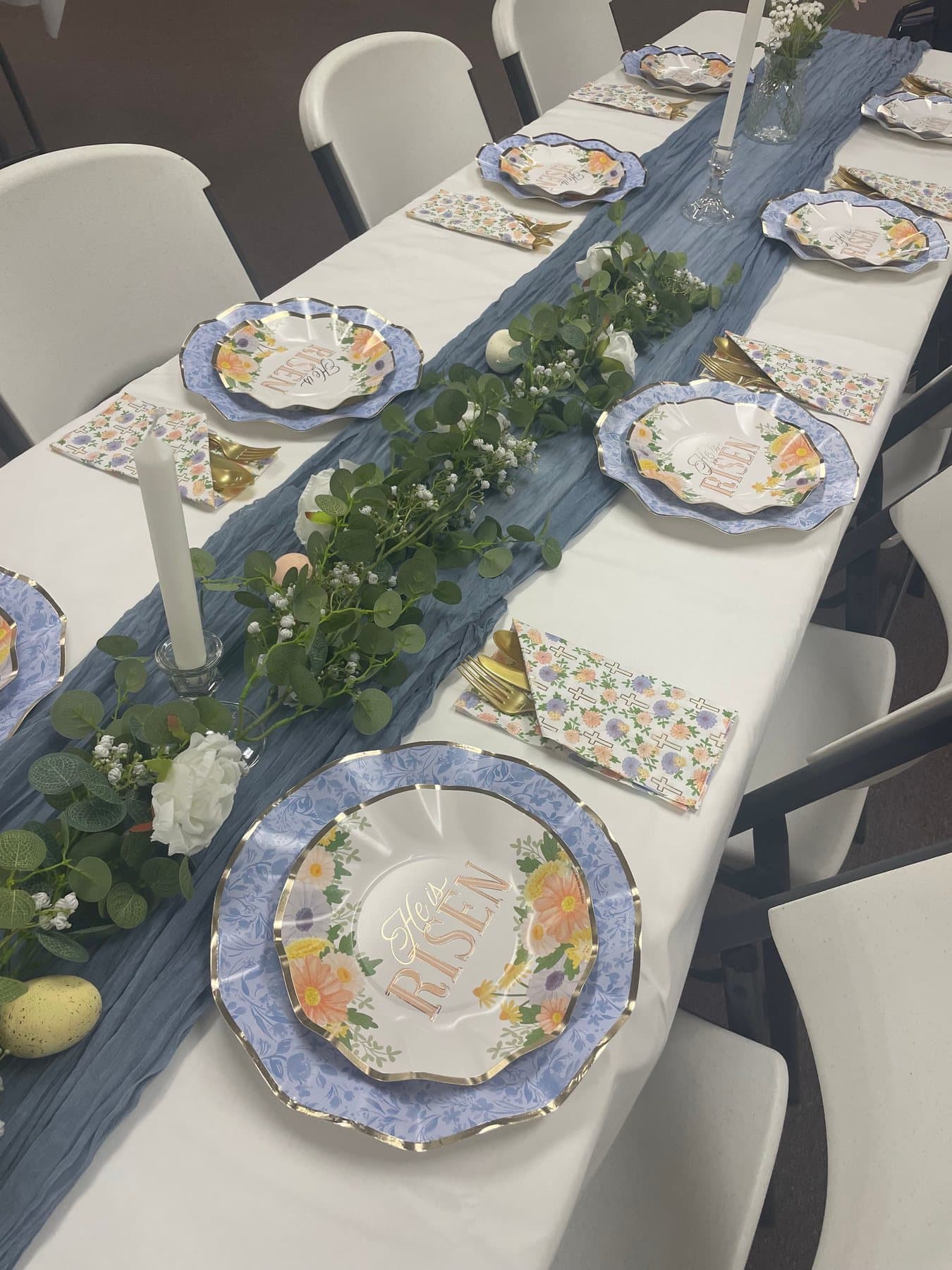 A lunch table set with floral plates, greenery and a blue runner