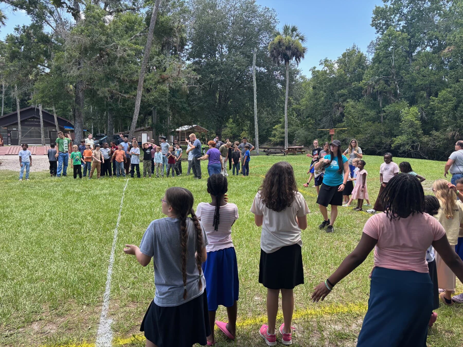 Children and adults playing a group game outside under the trees
