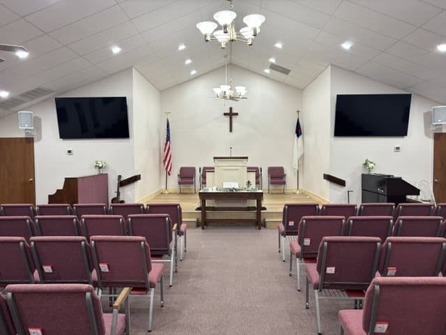 The sanctuary after the rebuild: burgundy chairs, a new wood platform, a wooden cross on the white wall