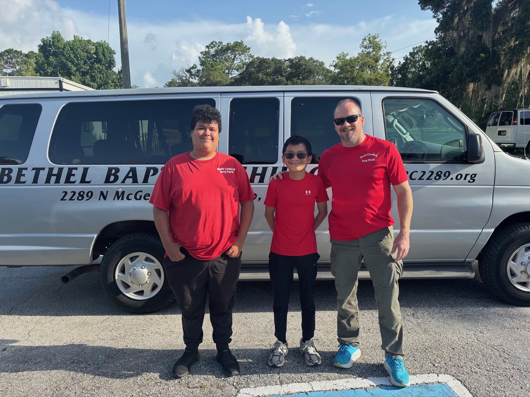 Three members in red shirts in front of the Bethel Baptist Church van